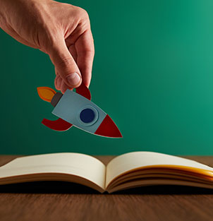 Hand holding a paper rocket over a book